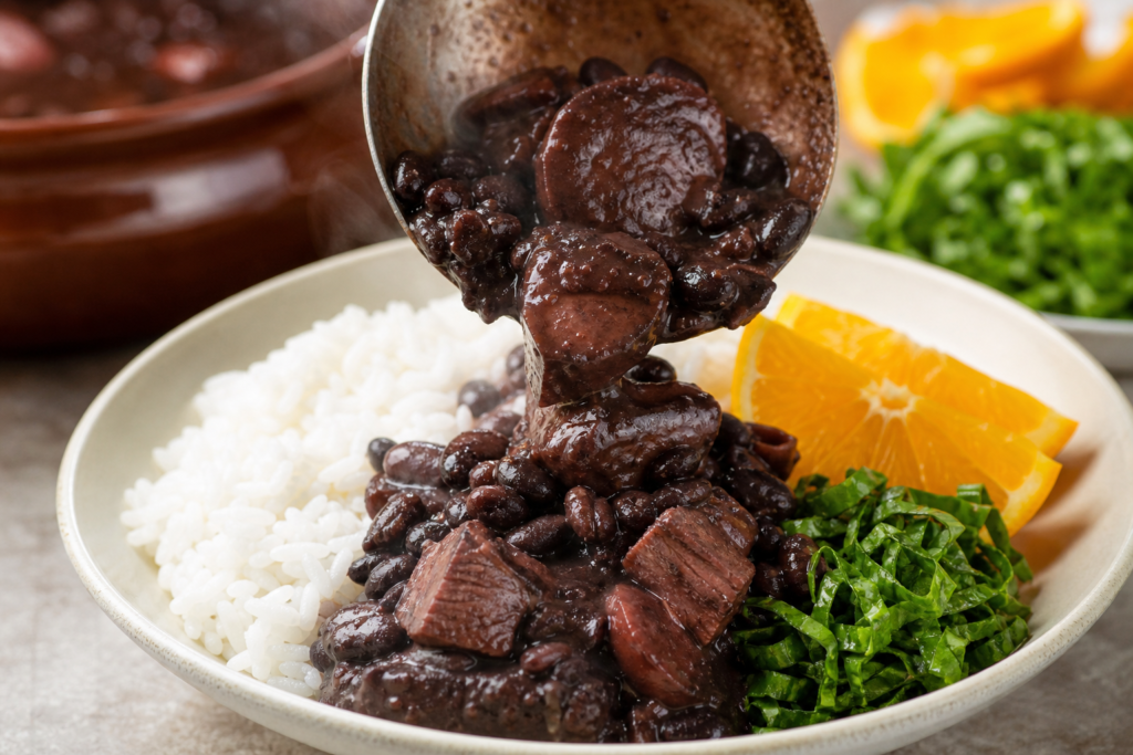A spoonful of feijoada being served over white rice with orange slices and shredded collard greens.
