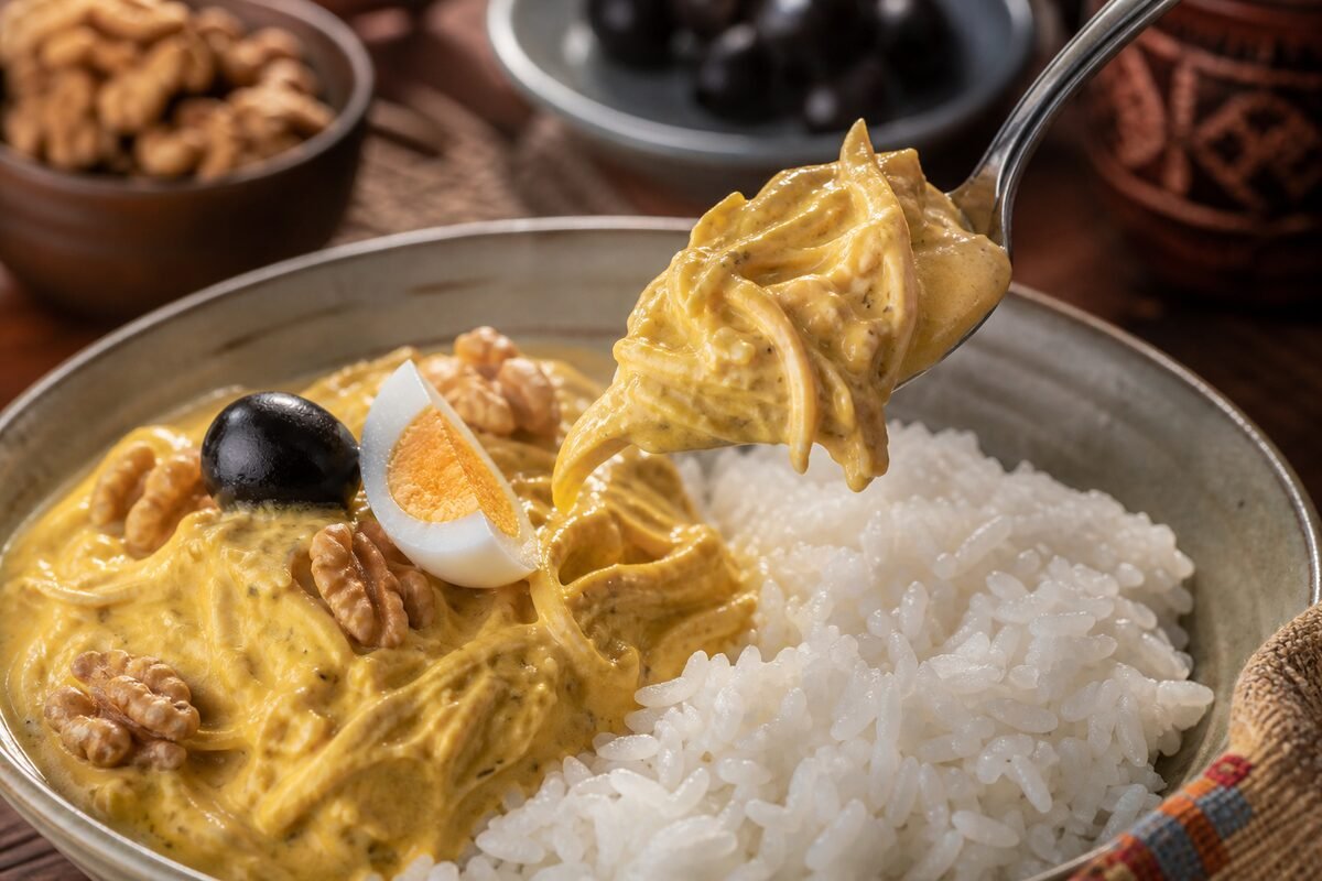 Close serving of Peruvian aji de gallina showing creamy yellow chicken sauce over rice with egg, olives, and walnuts.