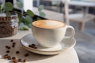 A velvety Australian flat white in a ceramic cup with espresso crema, microfoam, and coffee beans.