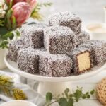 Chocolate-coated Australian lamingtons covered in coconut on a cake stand.