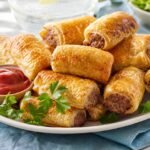 Golden Australian sausage rolls arranged on a platter with tomato sauce and parsley.