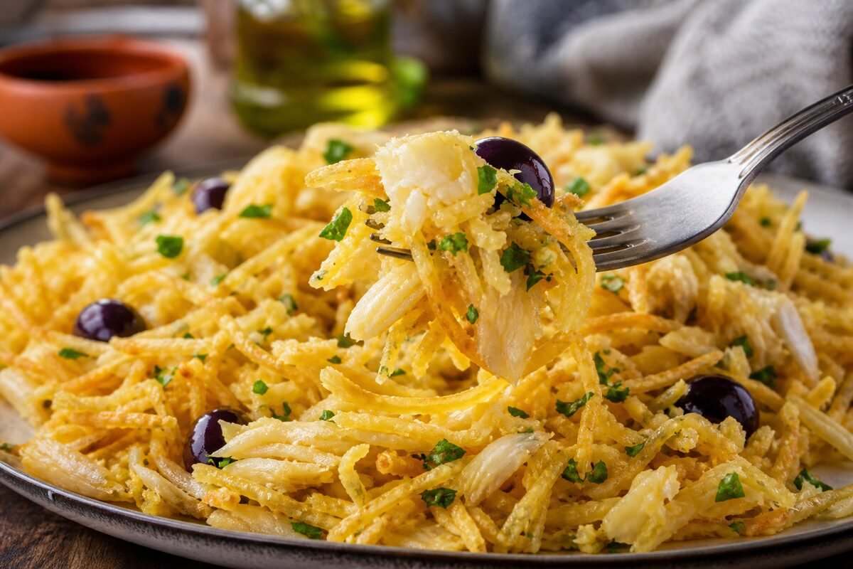 Close serving of Portuguese bacalhau a Bras showing tender cod, silky egg, crisp potatoes, olives, and parsley.