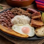 Colombian bandeja paisa with red beans, rice, ground beef, chicharron, fried egg, plantain, avocado, and arepa.