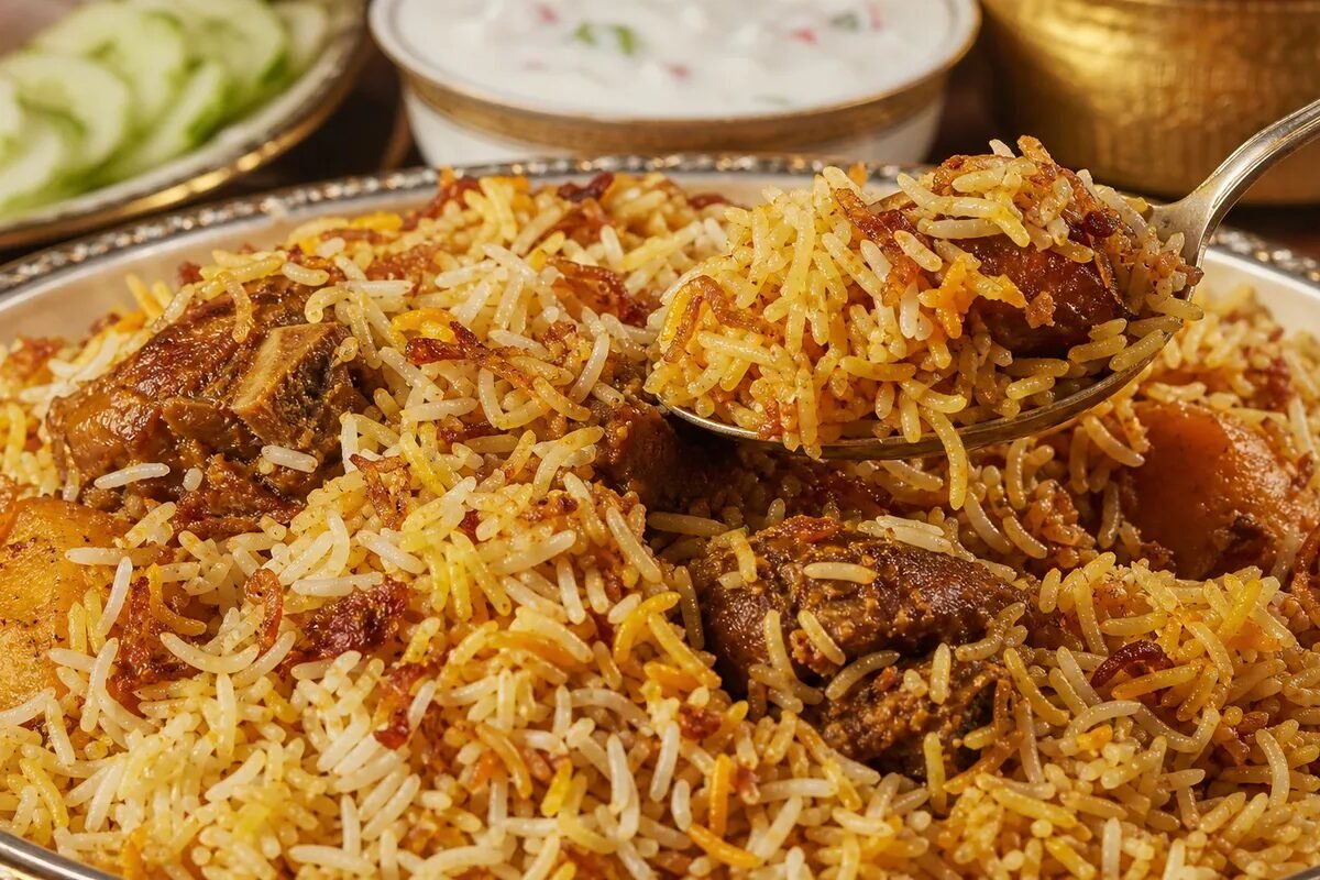 A close-up serving of Bangladeshi kacchi biryani with mutton, spiced rice, potato, and fried onion.