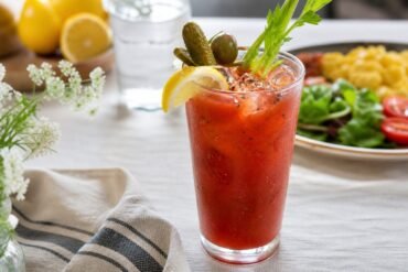 A classic Bloody Mary in a chilled glass with celery, lemon, cracked pepper, and ice on a brunch table.