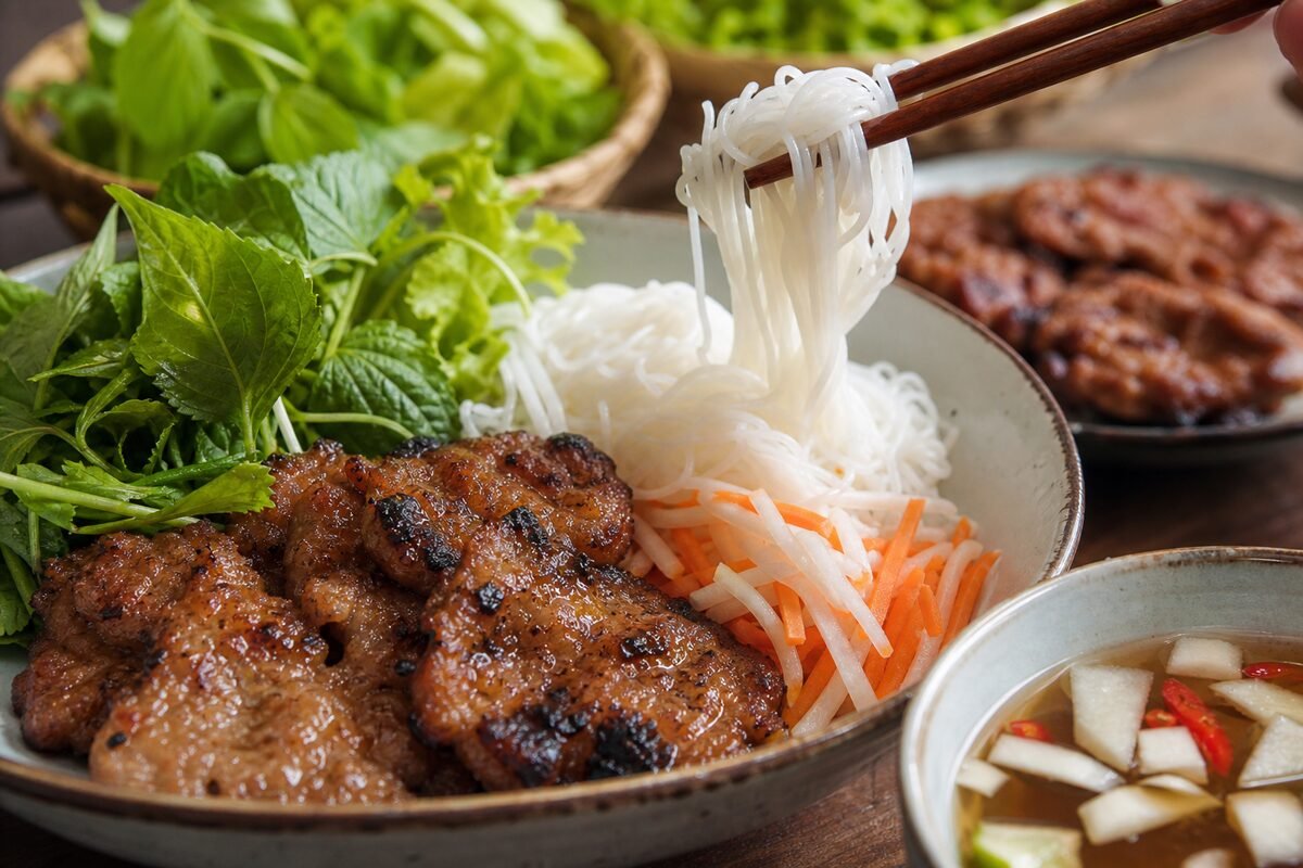 Close serving of Vietnamese bun cha with grilled pork, rice noodles, herbs, pickles, and dipping sauce.