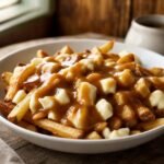 Canadian poutine with crisp golden fries, fresh cheese curds, and glossy brown gravy in a white bowl.