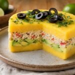 Layered Peruvian causa rellena with yellow potato, chicken, avocado, olives, and herbs on a ceramic plate.
