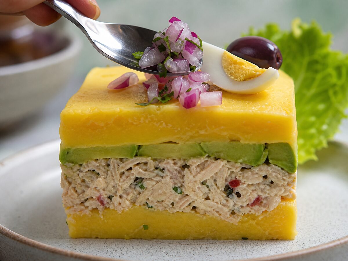A close-up wedge of Peruvian causa rellena showing potato, avocado, and seasoned chicken layers.
