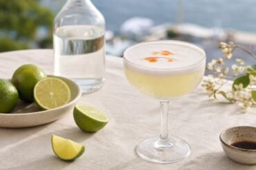 A chilled Chilean pisco sour in a coupe glass with frothy foam, lime, and aromatic bitters.