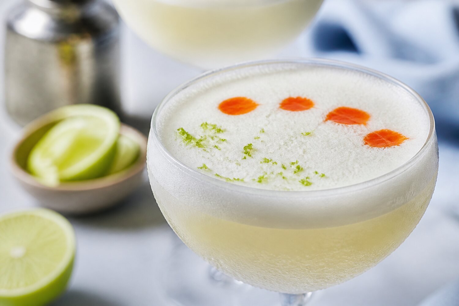 Close-up Chilean pisco sour with creamy foam, bitters, lime zest, and condensation.