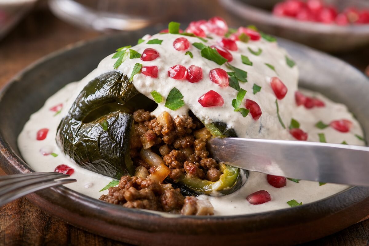 Close serving of Mexican chiles en nogada showing picadillo inside a roasted poblano under walnut sauce and pomegranate.