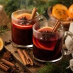 Steaming ruby-red mulled wine with orange slices, cinnamon, star anise, and cloves in clear mugs.