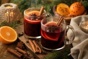 Steaming ruby-red mulled wine with orange slices, cinnamon, star anise, and cloves in clear mugs.