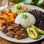 A Costa Rican casado plate with grilled chicken, rice, black beans, fried plantains, cabbage salad, and avocado.