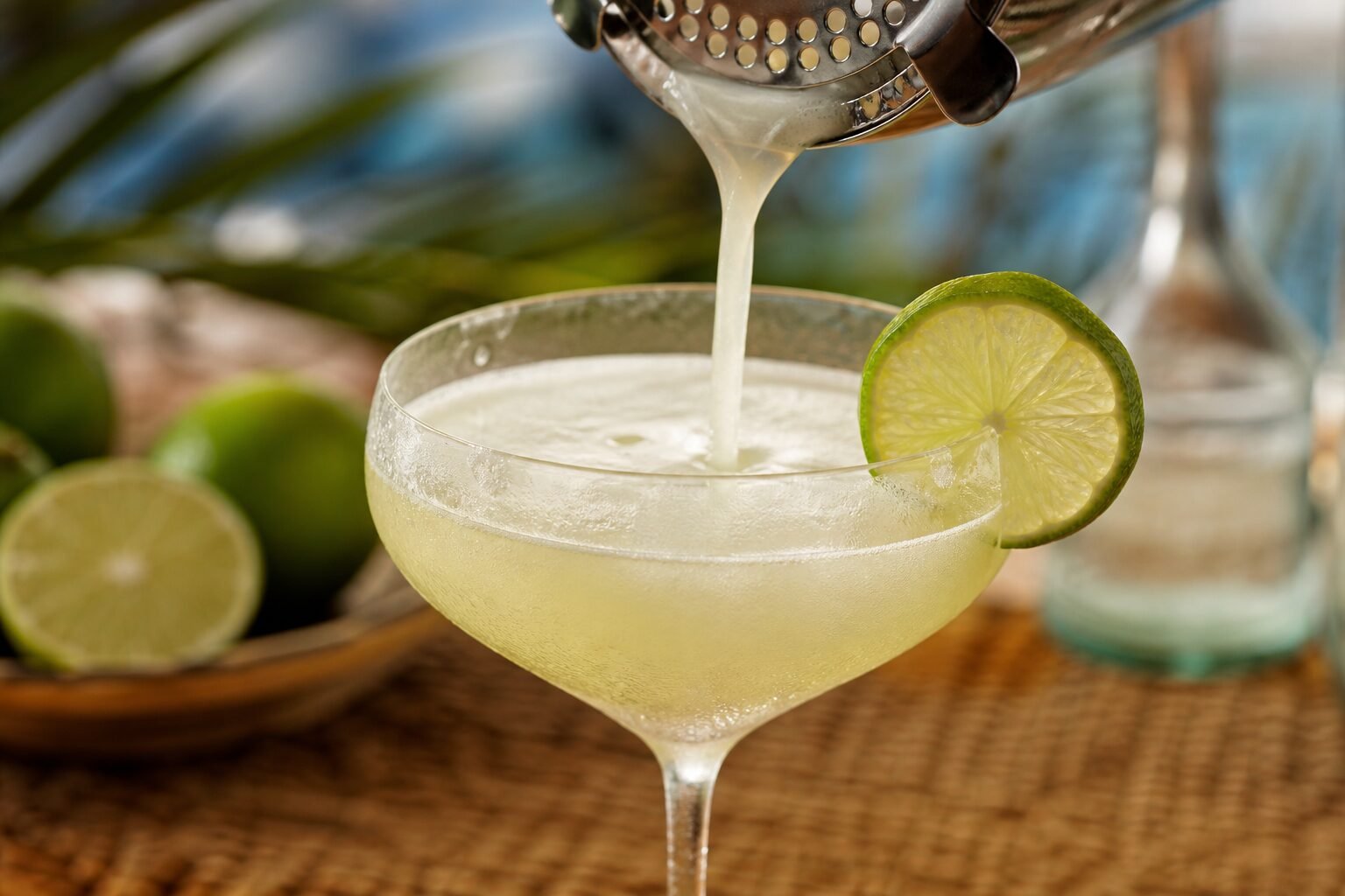 A frothy Cuban daiquiri being strained into a chilled coupe with a fresh lime wheel.