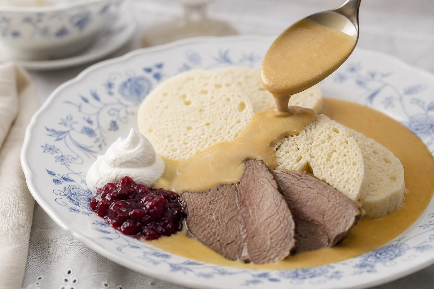 Czech svíčková being served with creamy sauce, bread dumplings, cranberry relish, and whipped cream.