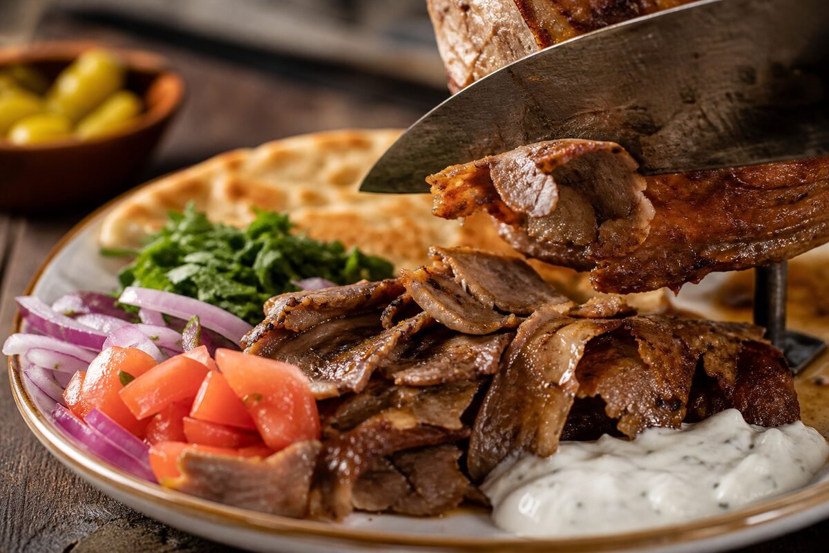Close view of sliced Turkish doner kebab with crisp meat edges, flatbread, vegetables, and garlic yogurt sauce.