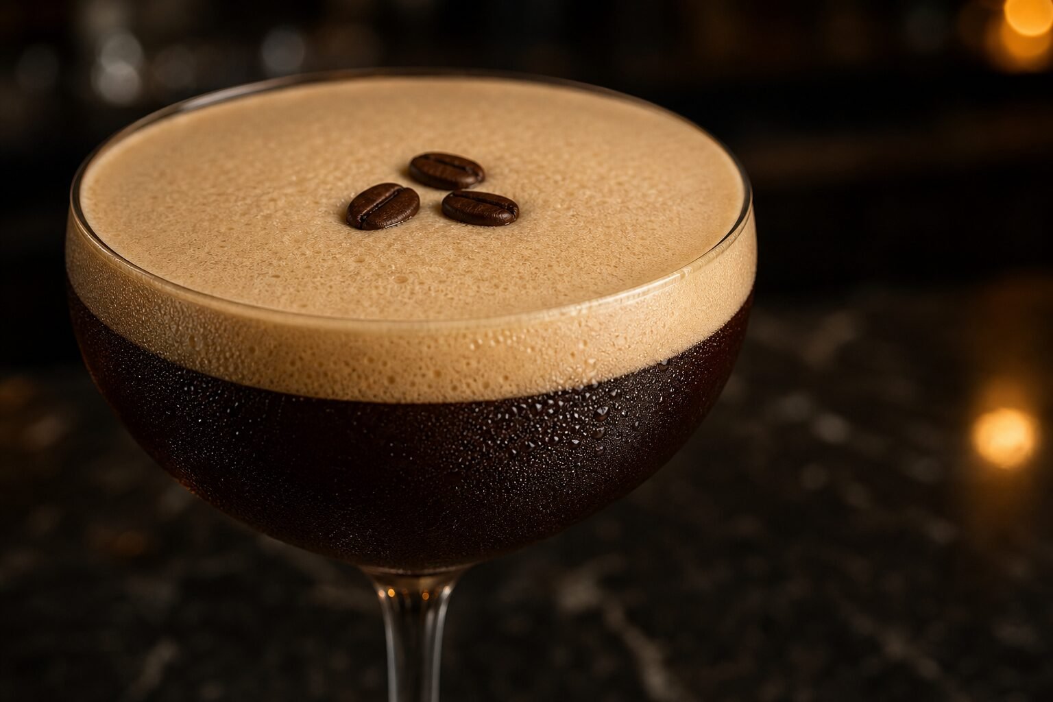 Close view of an Espresso Martini showing fine-bubbled crema, condensation, and three coffee beans.