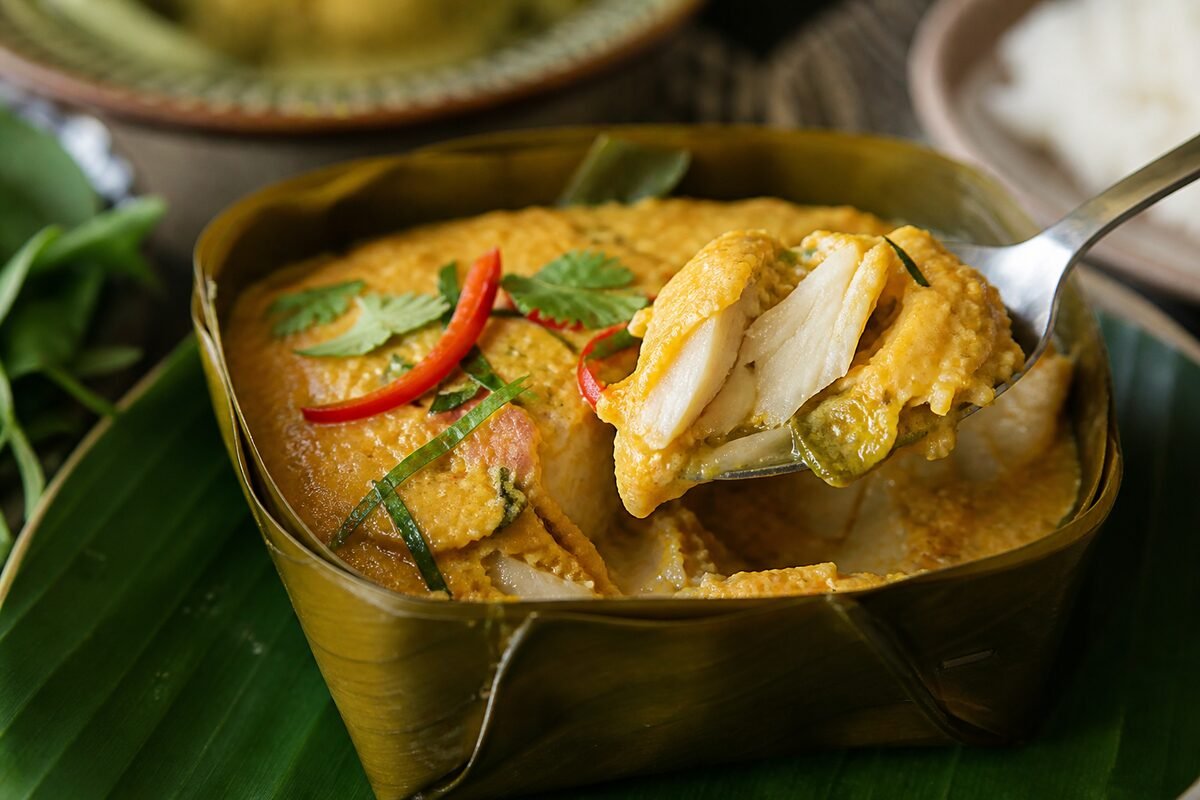 Close serving of Cambodian fish amok showing flaky fish, coconut curry custard, kaffir lime, and herbs.