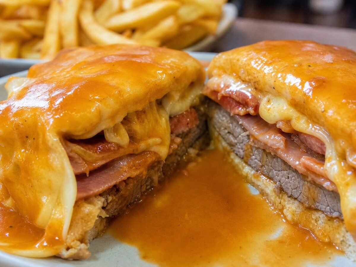 A close-up sliced Francesinha showing bread, steak, ham, sausage, melted cheese, and rich sauce.