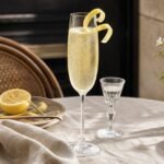 A pale gold French 75 cocktail with fine bubbles and a lemon twist in a champagne flute.