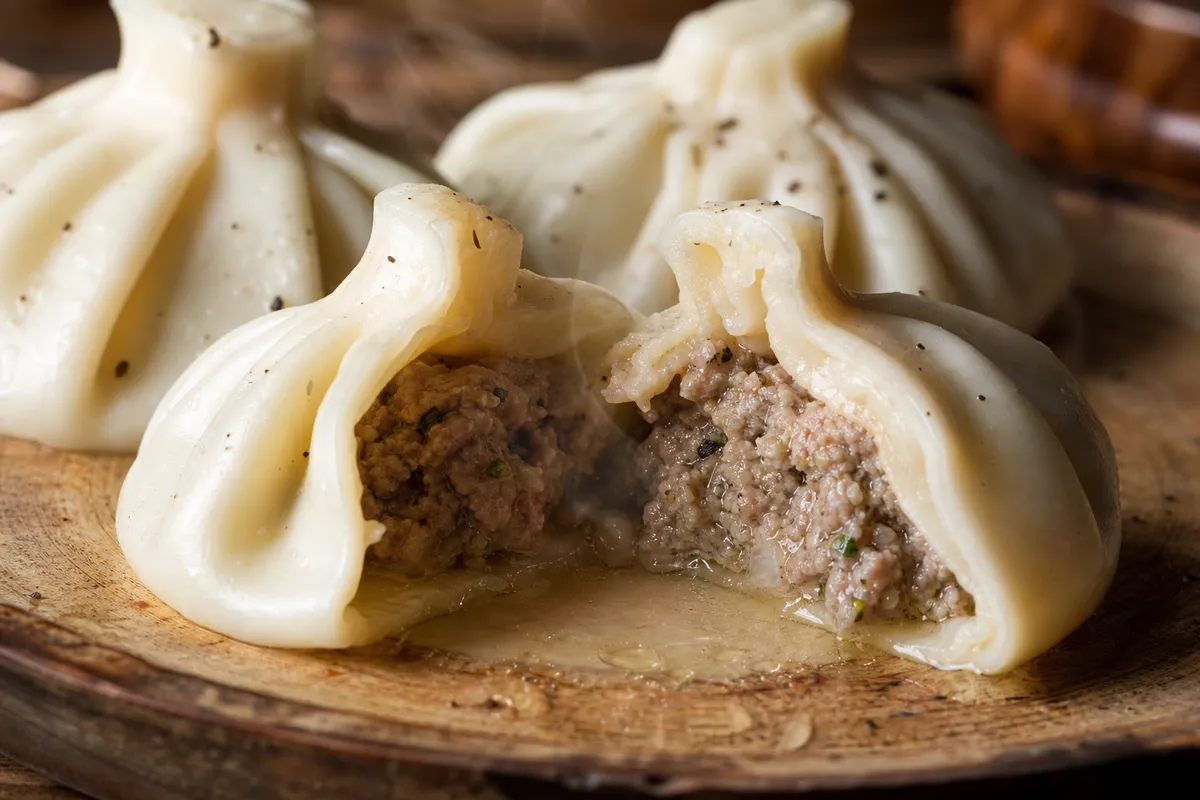 A close-up Georgian khinkali dumpling cut open to show its juicy meat filling and broth.