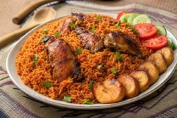 Ghanaian jollof rice with tomato-pepper rice, chicken, golden fried plantain, vegetables, and herbs.