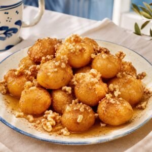 Greek loukoumades golden honey doughnuts with walnuts and cinnamon on a ceramic plate.