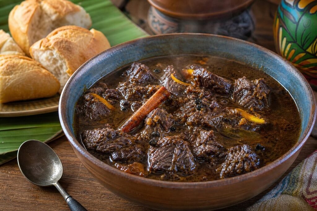 A bowl of glossy Guyanese pepperpot beef stew with bread on an earthy wooden table.