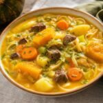 A bowl of Haitian soup joumou with pumpkin broth, beef, cabbage, carrots, potatoes, pasta, and herbs.