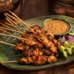 Charred Indonesian chicken satay skewers with peanut sauce, cucumber, onion, and lime.