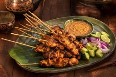 Charred Indonesian chicken satay skewers with peanut sauce, cucumber, onion, and lime.