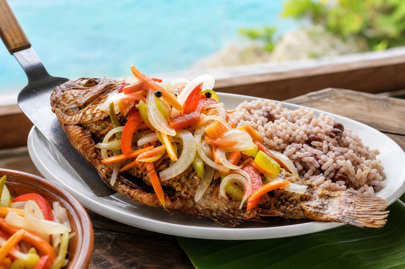Crisp Jamaican escovitch fish being plated with colorful pickled vegetables and rice.