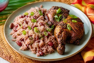 Jamaican rice and peas with coconut, red kidney beans, thyme, scallions, and jerk-seasoned chicken on a plate.