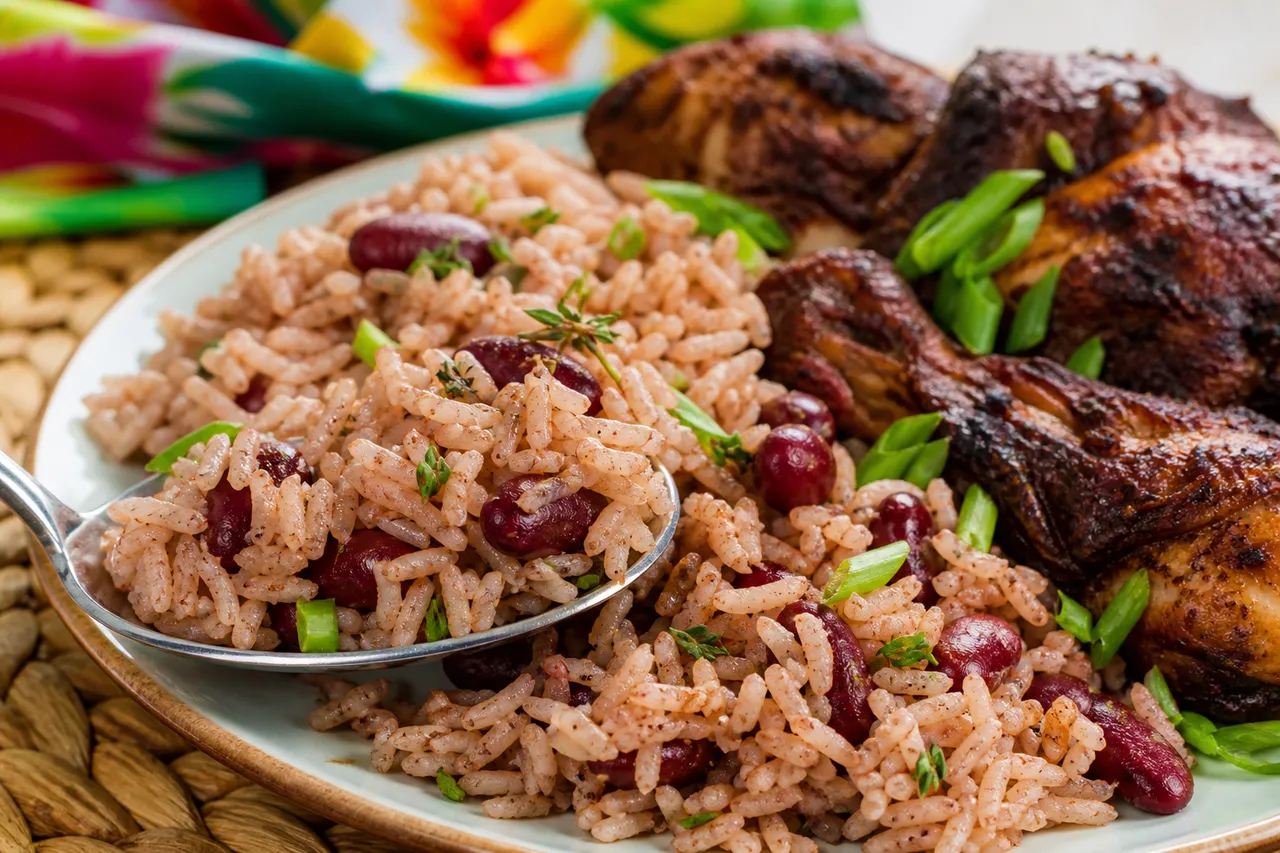A close-up spoonful of Jamaican rice and peas with fluffy grains, red kidney beans, thyme, scallions, and jerk chicken.