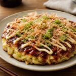 A Japanese okonomiyaki savory cabbage pancake topped with sauce, mayonnaise, bonito flakes, and scallions.