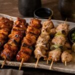 Japanese yakitori chicken skewers with tare glaze, scallions, and lemon on a ceramic platter.