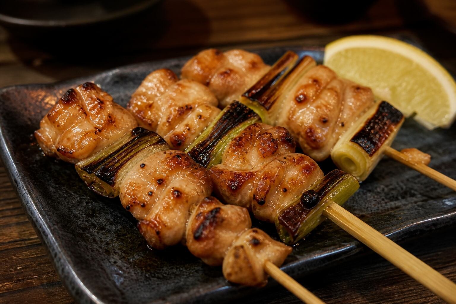 Close serving of charred Japanese yakitori chicken skewers with glossy tare and scallions.