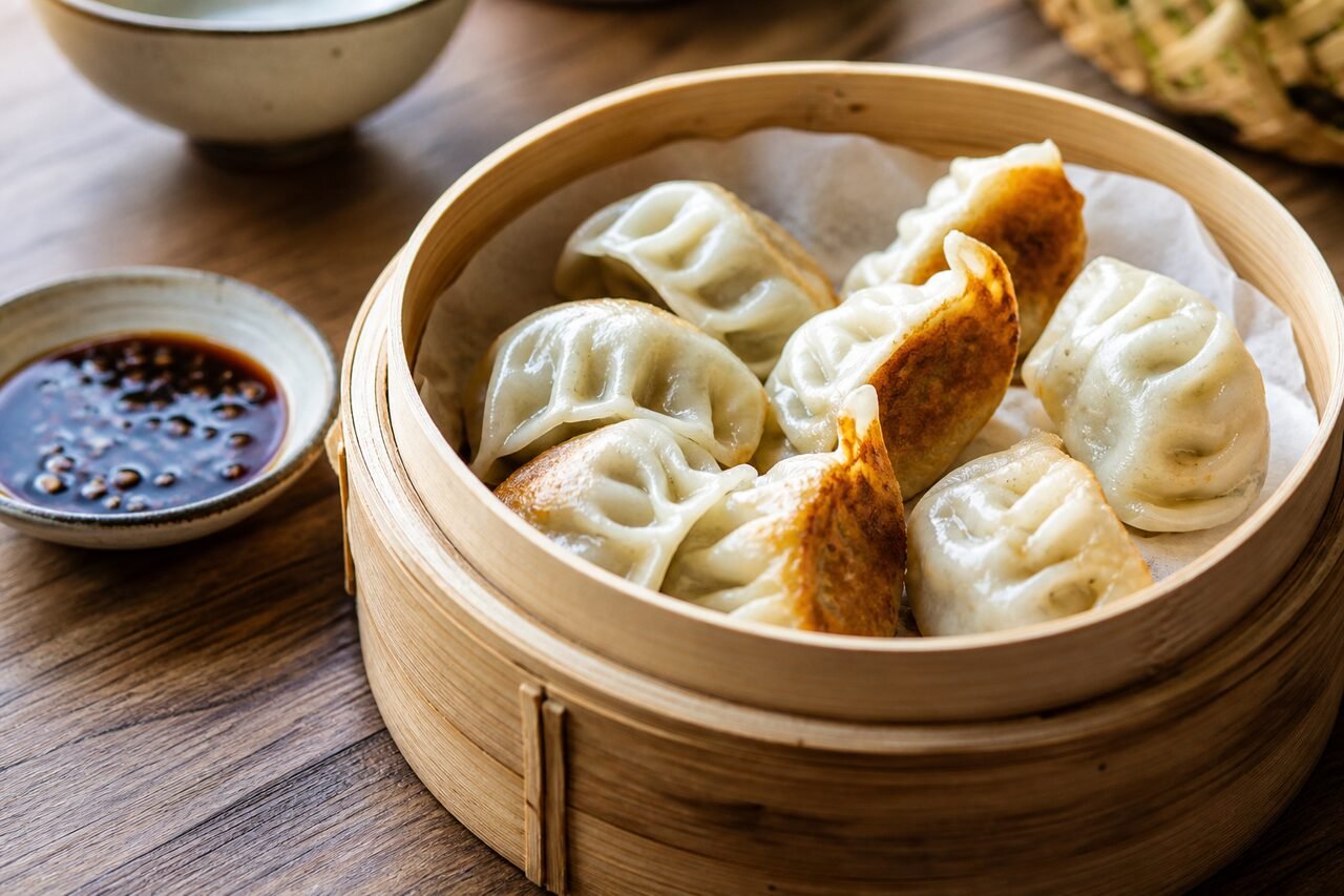 Close serving of Chinese jiaozi dumplings in a bamboo steamer beside dipping sauce.