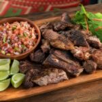 A platter of Kenyan nyama choma grilled meat with kachumbari, greens, and lime.