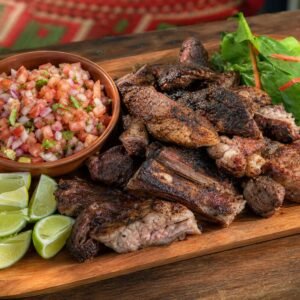 A platter of Kenyan nyama choma grilled meat with kachumbari, greens, and lime.