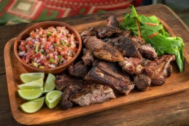 A platter of Kenyan nyama choma grilled meat with kachumbari, greens, and lime.