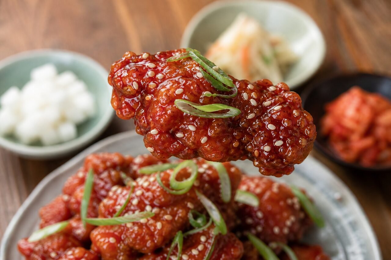 Close serving of glossy Korean fried chicken with sesame seeds, scallions, and pickled radish.