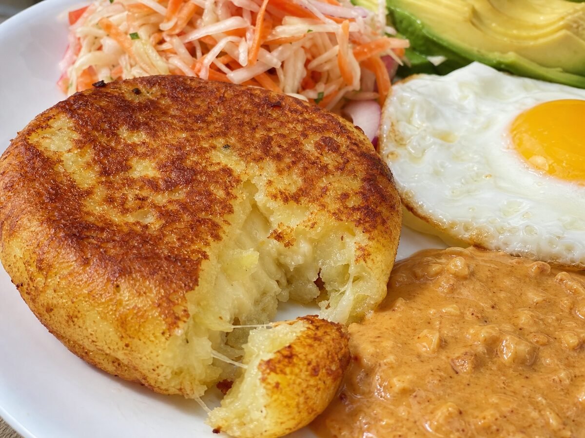 A close-up Ecuadorian llapingacho showing its crisp potato crust and cheesy center with peanut sauce.