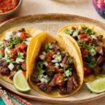 Three Mexican beef tacos in corn tortillas with cilantro, onion, salsa, and lime wedges.