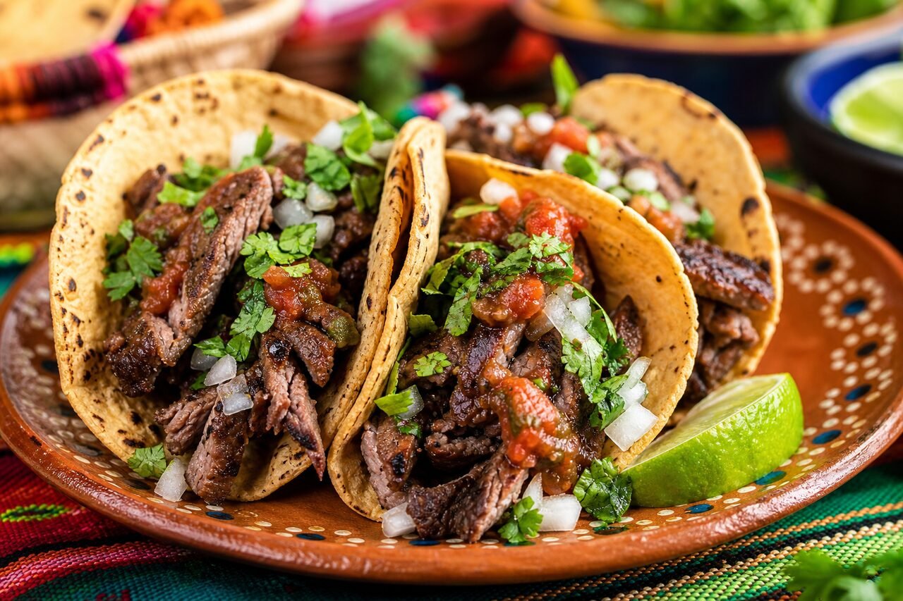 Close serving of Mexican beef tacos with charred beef, onion, cilantro, salsa, and lime.