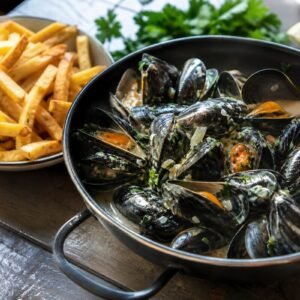 Belgian moules-frites with steamed mussels in creamy white wine broth beside crisp golden fries and parsley.