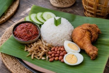 Malaysian nasi lemak with coconut rice, sambal, anchovies, peanuts, cucumber, egg, and fried chicken.