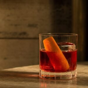 A ruby-red Negroni cocktail with clear ice and a wide orange peel in a rocks glass.